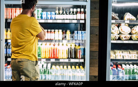 L'uomo solo e isolato al supermercato o minimarket scegliendo il suo drink o snack in grande frigorifero con un sacco di prodotti - difficile selezionare e scegliere Foto Stock
