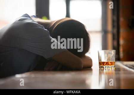 Bevuto giovane donna che dorme sul bancone bar vicino al bicchiere di Whiskey Foto Stock