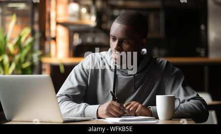 Focalizzato giovane studiando con il computer portatile di prendere appunti in cafe Foto Stock