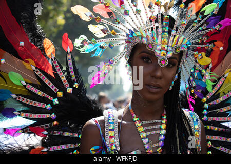 Primo piano di una performer femminile in un vestito luminoso con piume e colori urlanti visto al carnevale di Notting Hill 2019. Foto Stock