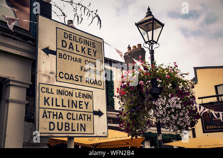 Vecchio Irish cartello stradale per Dalkey, Killiney e Dublino situato nel villaggio di Dalkey sulla lingua inglese e lingue irlandese. Foto Stock