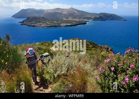 L'Italia, Sicilia e Isole Eolie, classificato come patrimonio mondiale dall UNESCO, Isola di Lipari, escursionisti sulla via costiera e isola di Vulcano in background Foto Stock