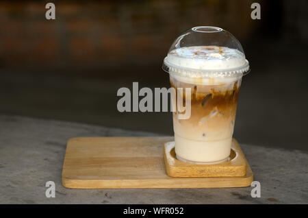 Caffè ghiacciato con crema di latte in un bicchiere di plastica è su un piattino di legno, fuoco selettivo, latte art Foto Stock