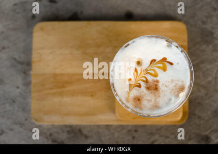 Caffè ghiacciato con crema di latte in un bicchiere di plastica è su un piattino di legno, fuoco selettivo, latte art Foto Stock