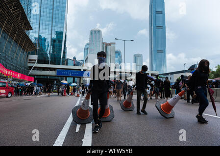 Manifestanti trascinare traffico coni per essere usati come barricate improvvisate durante la dimostrazione.contro gli ordini di polizia, migliaia di governo anti-manifestanti hanno marciato attraverso strade. Scontri con la polizia ha provocato decine di gas lacrimogeni turni e proiettili essendo sparati, portando infine a più arresti. Nonostante la continua pressione da manifestanti, il governo di Hong Kong ha ancora alla grotta per i manifestanti la domanda di completamente il ritiro della legge in materia di estradizione. Foto Stock