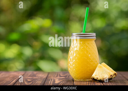 Ananas fresco succo in un barattolo di vetro sul tavolo in legno all'esterno. Estate bevanda rinfrescante Foto Stock