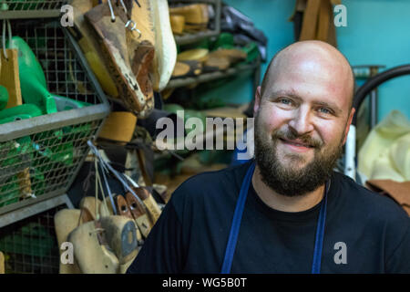 Ritratto di un muso da parte calva con la barba, calzolaio cercando fotocamera presso la sua officina sorridente. Foto Stock