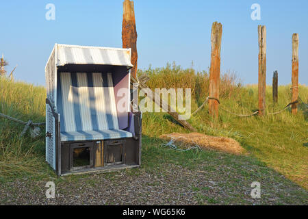 Coperto e Spiaggia di vimini sedia davanti di pali in legno e le dune di sabbia con erba vicino alla spiaggia di Isola di Texel in Paesi Bassi Foto Stock