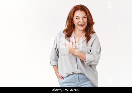 Fiducioso di mezza età redhead donna europea che raccontano interessante prodotto consiglia di check-out promo toothy sorridente sicuri di sé rivolta verso sinistra ind Foto Stock