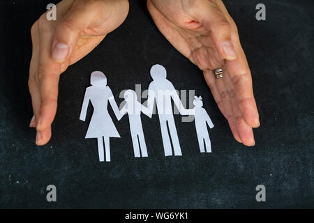 Vista in elevazione di una mano umana della protezione della famiglia carta tagliato su Foto Stock