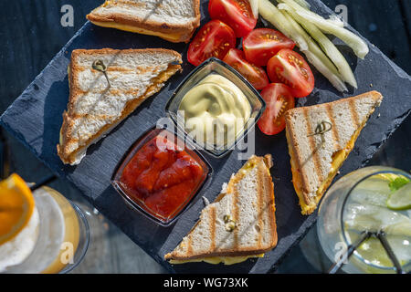 Club sandwich con prosciutto e formaggio e pomodoro rosso su nero ardesia piastra. Prosciutto Formaggio cheddar toast. Fetta di pane con prosciutto, formaggio, mostarda e salsa di pomodoro Foto Stock