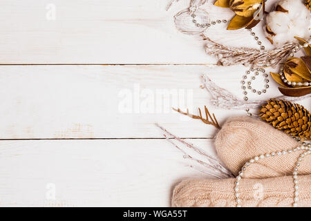 Closeup beige caldo guanti a maglia, perline, ramoscelli e coni bianchi su sfondo di legno con copia spazio, vista dall'alto. Vestiti da donna. Lay piatto. Inverno accogliente, Foto Stock