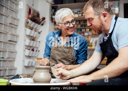 Donna senior di argilla di filatura su una ruota con un aiuto di un insegnante di classe in ceramica Foto Stock