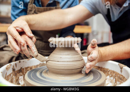 Donna senior di argilla di filatura su una ruota con un aiuto di un insegnante di classe in ceramica Foto Stock