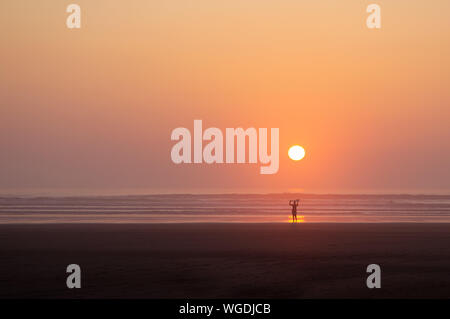 La silhouette di una donna che porta una tavola da surf sulla sua testa come lei cammina fuori del mare. Con il tramonto dietro di lei. Saunton Sands, Devon, Regno Unito Foto Stock