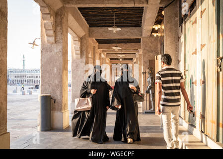 Doha, Qatar - 3 DIC 2016: due donne che indossano abayas sono a piedi verso il basso di uno dei souq passaggio mentre un uomo indiano è passando da guardando a loro. Tak Foto Stock