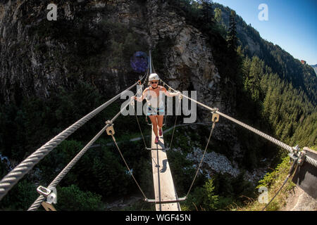 Una donna si sale la via ferrata sopra Lac de la rosière accanto al francese stazione sciistica di Courchevel nelle Alpi durante l'estate. Ponte di corde. Foto Stock