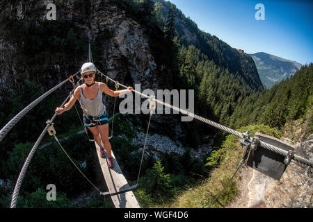 Una donna si sale la via ferrata sopra Lac de la rosière accanto al francese stazione sciistica di Courchevel nelle Alpi durante l'estate. Ponte di corde. Foto Stock