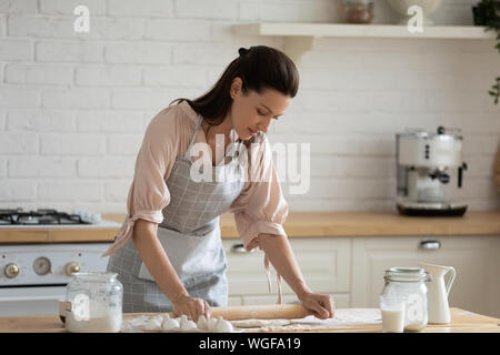 Casalinga in piedi su tavolo da cucina appiattire la pasta con il mattarello Foto Stock