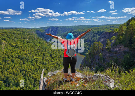 La donna salì sulla cima della montagna, fare escursionismo, essa gioisce nella sua vittoria, alzando le mani verso l'alto. Di fronte a lei, qui di seguito è una vasta foresta Foto Stock