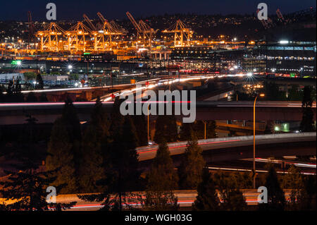 Porto di Seattle al tramonto con grandi gru in una fila con i-5 sovrappassi. Foto Stock