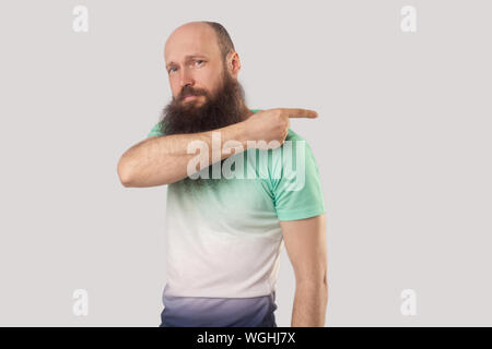 Fuori dalla mia faccia. Ritratto di angry medio di età compresa tra uomo calvo con barba lunga in verde chiaro t-shirt standing, cerca e mostra l'uscita modo. indoor studi Foto Stock