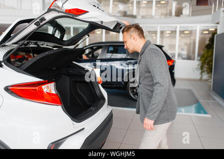 L'uomo guarda il tronco della nuova vettura in showroom Foto Stock