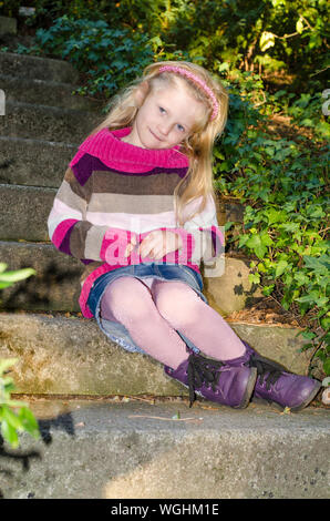 Ritratto di ragazza carina nel cappuccio nella magica atmosfera autunnale in posa di parco verde pieno di foglie cadute, Foto Stock