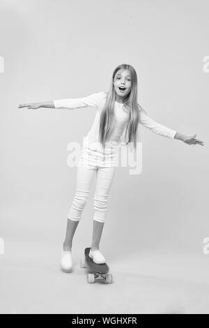 Rigenerare la sua energia lo skateboard. Adorabile bambina eseguendo acrobazie con lo skateboard su sfondo rosa. Carino piccola ragazza lo skateboard su viola penny board. Andare al giorno per la corsa su skateboard. Foto Stock