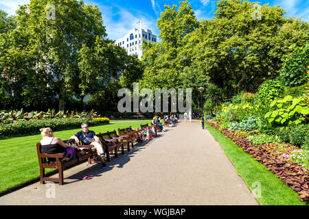 La gente seduta sulle panchine in estate a Victoria Embankment Gardens, London, Regno Unito Foto Stock