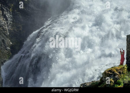 Rosso vestito donna è un Huldra, fata, saga figura, cascata Kjosfossen, cascata vicino Fureberget, ballerino in abito rosso, pareti rocciose, Flåm, Sogn og Fjo Foto Stock