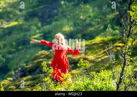 Rosso vestito donna è un Huldra, fata, saga figura, cascata Kjosfossen, cascata vicino Fureberget, ballerino in abito rosso, pareti di roccia, Flåm, Sogn og Fjo Foto Stock