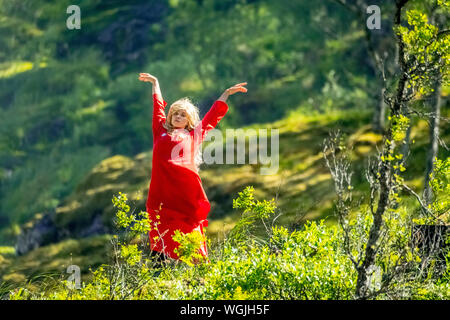 Rosso vestito donna è un Huldra, fata, saga figura, cascata Kjosfossen, cascata vicino Fureberget, ballerino in abito rosso, pareti di roccia, Flåm, Sogn og Fjo Foto Stock