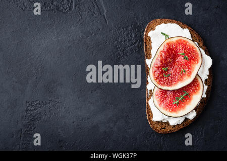 Fig e cottage cheese sul pane di segale tostato nero su sfondo di calcestruzzo. Vista superiore, spazio di copia Foto Stock