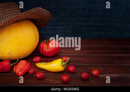 La Zucca in un cappello, sparsi in rosso dei pomodori e peperoni, uno giallo pepe. I pomodori sono piccolo e uno grande. Le schede sono marrone, uno sfondo da una sciarpa f Foto Stock