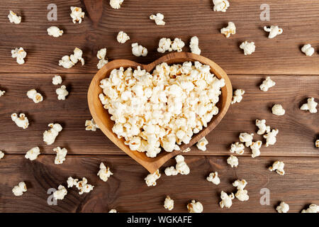 Il Popcorn in un marrone piatto di legno a forma di cuore su di un tavolo di legno. Il Popcorn è disposto sul tavolo Foto Stock