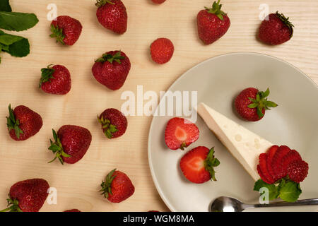 Una piastra con fragola e menta decorate cheesecake sorge su una luce tavolo in legno circondato da fragole Foto Stock