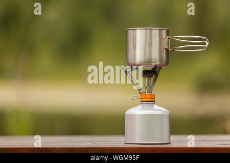 Il campeggio tazza di ferro con un bruciatore a gas naturale sfondo bokeh di fondo Foto Stock