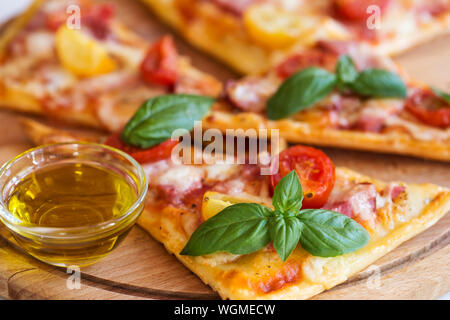 Fette di pizza con basilico e olio d'oliva sul piatto di legno Foto Stock
