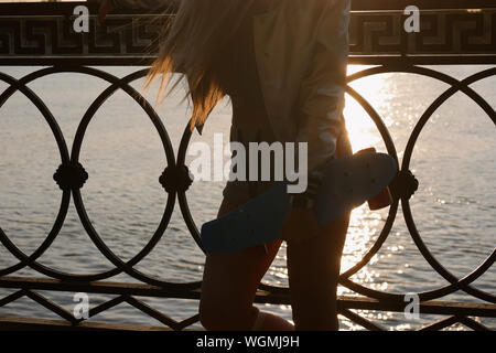 Retroilluminato sfocate colpo di giovane donna in esecuzione con scateboard nella luce del tramonto sul mare Foto Stock