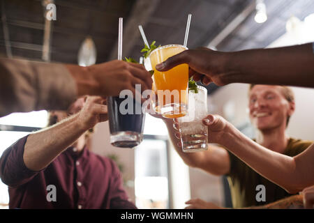 Angolo basso closeup di amici bicchieri tintinnanti seduti a tavola in cafe godendo il freddo bevande rinfrescanti, spazio di copia Foto Stock