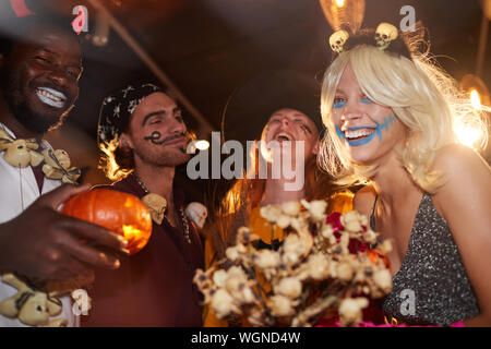 Basso angolo vista sul gruppo di amici gustando festa di Halloween in discoteca, concentrarsi su sorridente giovane donna avente fun Foto Stock