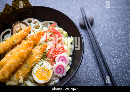 Close up della ciotola di giapponese gourmet udon noodle soup con Topping colorati di zenzero sott'aceto, uova sode, swirly narutomaki pattern, gamberi impanati Foto Stock