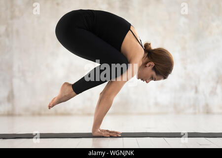 Attraente giovane donna a praticare yoga, facendo esercizio di gru, Bakasana Foto Stock