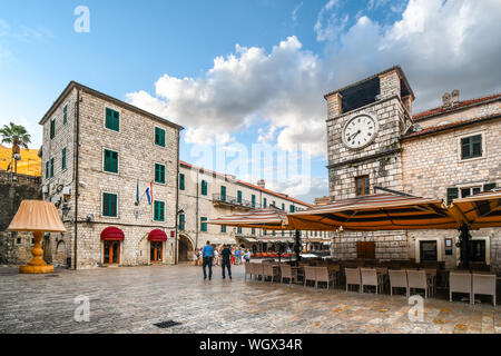 La mattina in Piazza dei bracci di Kotor Montenegro come turisti a piedi passato caffetterie lungo la strada e una lampada oversize mostra nella città vecchia medievale. Foto Stock