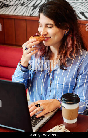 Piuttosto giovane femmina coder lavorando presso il cafe tavolo e maleodoranti ciliegio delizioso sbuffo sta andando ad avere per il dessert Foto Stock