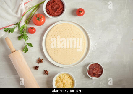 Pasta fresca la base della pizza e gli ingredienti su un tavolo bianco. Vista dall'alto. Foto Stock