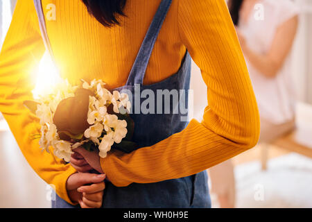 Close-up di un irriconoscibile ragazza adolescente nascondono bellissimi fiori dietro per la piacevole sorpresa di sua madre. La festa della mamma concept Foto Stock