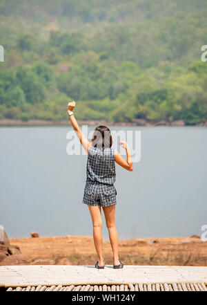 Donne alzando le braccia e sullo sfondo le montagne e acqua al serbatoio Chakrabongse , Prachinburi in Thailandia. Foto Stock