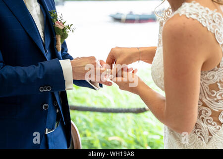 Dita della sposa scorrere l'oro anello di nozze sulla mano dello sposo Foto Stock